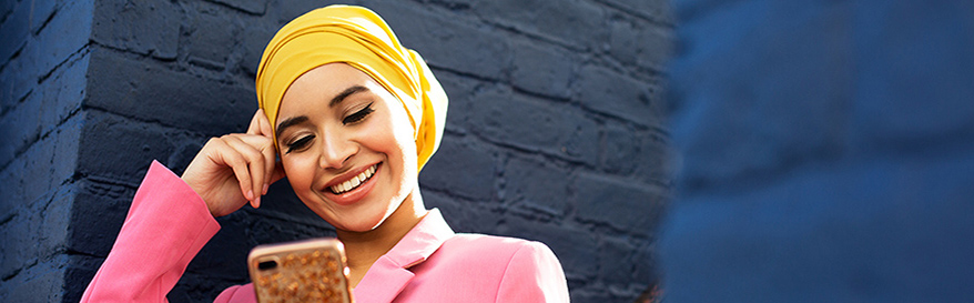 Woman with head dress looking at her cell phone and smiling